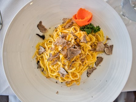 Wide white bowl with pasta noodles and shaved truffle on top